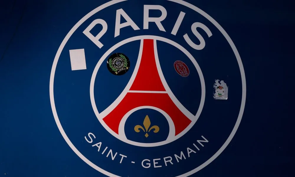 Jersey domicile PSG dengan warna biru, bande merah, dan bordur putih dalam sorotan suporter